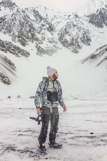 A rugged mountain climber wearing durable technical outerwear against a snowy peak backdrop.