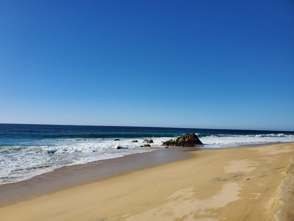 a sandy beach next to the ocean under a blue sky