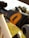 Close-up of a suspension component from a bicycle with a sleek design. The focus is on the black cylinder marked with an orange letter 'E', suggesting a brand or model. The background is blurred, showcasing what seems to be sunlight filtering through trees.