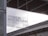 A modern architectural setting features signage with text that reads 'HYUNDAI MOTORSTUDIO BUSAN GMC'. The signage is placed against a backdrop of a contemporary building with visible structural and glass elements. The lighting creates a contrast between the dark edges of the structure and the bright, overcast sky.
