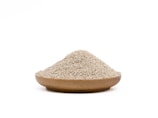 A wooden bowl filled with a mound of small, beige grains rests against a plain white background.