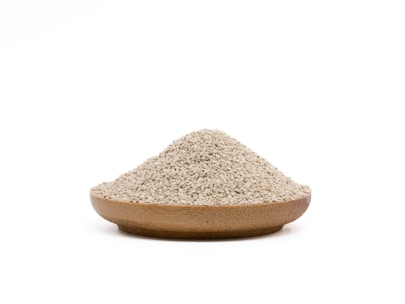 A wooden bowl filled with a mound of small, beige grains rests against a plain white background.