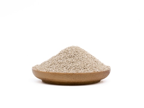 A wooden bowl filled with a mound of small, beige grains rests against a plain white background.