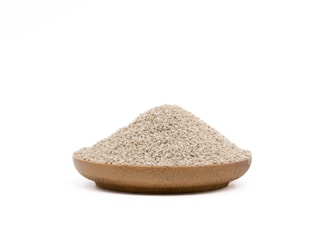 A wooden bowl filled with a mound of small, beige grains rests against a plain white background.