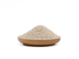 A wooden bowl filled with a mound of small, beige grains rests against a plain white background.