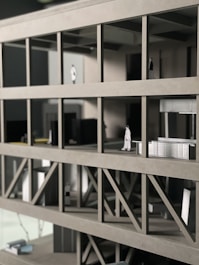 A scale architectural model of a building with multiple floors, featuring structural beams and small figurines representing people. The model is made of gray materials, indicating a modern design concept.