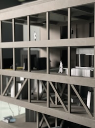 A scale architectural model of a building with multiple floors, featuring structural beams and small figurines representing people. The model is made of gray materials, indicating a modern design concept.