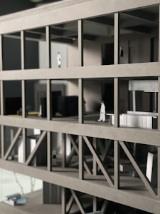 A scale architectural model of a building with multiple floors, featuring structural beams and small figurines representing people. The model is made of gray materials, indicating a modern design concept.