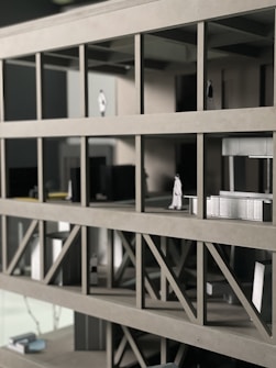 A scale architectural model of a building with multiple floors, featuring structural beams and small figurines representing people. The model is made of gray materials, indicating a modern design concept.