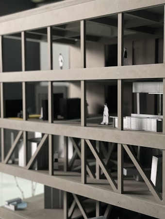 A scale architectural model of a building with multiple floors, featuring structural beams and small figurines representing people. The model is made of gray materials, indicating a modern design concept.