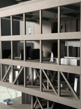A scale architectural model of a building with multiple floors, featuring structural beams and small figurines representing people. The model is made of gray materials, indicating a modern design concept.