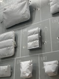 Various white pouches and bags of different sizes are displayed on a light-colored background with numbered sections. Each bag has a minimalistic design with labels attached.