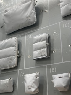 Various white pouches and bags of different sizes are displayed on a light-colored background with numbered sections. Each bag has a minimalistic design with labels attached.