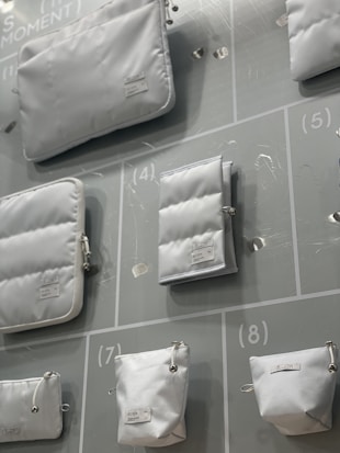 Various white pouches and bags of different sizes are displayed on a light-colored background with numbered sections. Each bag has a minimalistic design with labels attached.