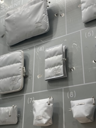 Various white pouches and bags of different sizes are displayed on a light-colored background with numbered sections. Each bag has a minimalistic design with labels attached.