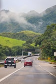 a group of cars driving down a road with mountains in the background
