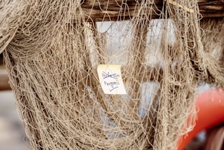 A large, tangled fishing net is hung over a wooden beam. A small yellow sticky note that reads 'Perfection in Progress' is attached to the netting.