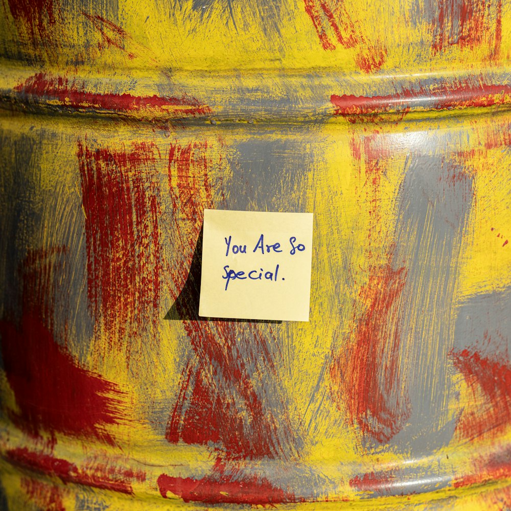 a yellow and red painted barrel with a note attached to it