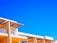 A modern architectural structure with an angular, geometric design set against a vivid blue sky. The building features light, peach-colored walls and large, glass windows, with a decorative lattice roof overhanging some of the windows.