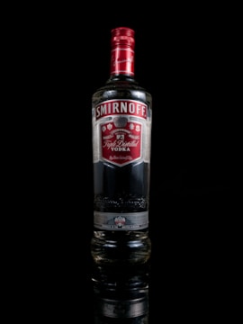 A bottle of Smirnoff vodka with a red cap and label against a black background. The label features silver and white detailing, with clear branding and text visible.