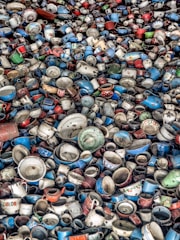 A large collection of vintage and colorful enamel mugs, pots, and kitchenware tightly packed together. The dishware is a mix of various shades including blue, red, white, and green, with some showing floral patterns or labels.