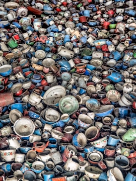 A large collection of vintage and colorful enamel mugs, pots, and kitchenware tightly packed together. The dishware is a mix of various shades including blue, red, white, and green, with some showing floral patterns or labels.