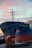 A large cargo ship, named the Fairchem Integrity, is docked at a port. Water is seen flowing from the side of the vessel near the front. The sky is filled with pink and blue hues typical of either a sunrise or sunset. The ship's hull is dark blue with some red near the waterline.