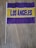 A small flag with the words 'Los Angeles' written in bold purple letters on a yellow background, surrounded by a purple design. The flag is attached to a wooden stick and is placed on a wooden floor.
