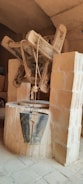 A traditional stone well featuring a wooden pulley system with ropes is situated indoors. A vintage, weathered metal bucket hangs from the ropes, indicating a rustic and historical setting. The surrounding area is constructed from rough-hewn stone blocks.