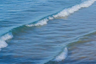 Soft aqua blue waves gently rolling onto a cream-colored shore, evoking calm and renewal.