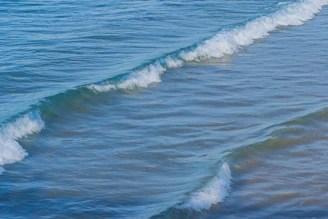Soft aqua blue waves gently rolling onto a cream-colored shore, evoking calm and renewal.