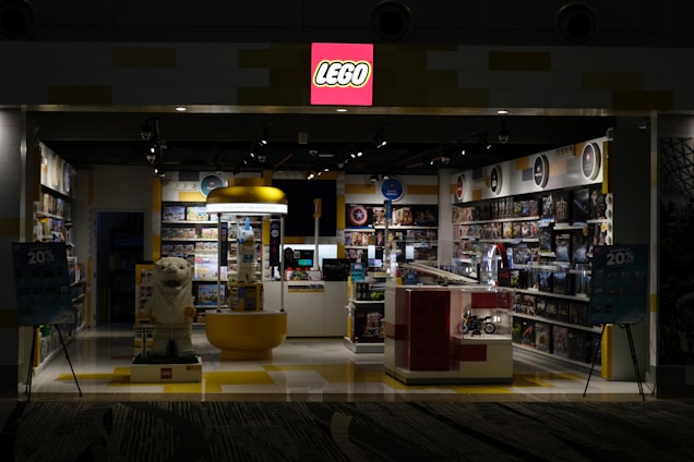 Cozy toy store corner with colorful Lego® and Playmobil® sets displayed invitingly on wooden shelves.