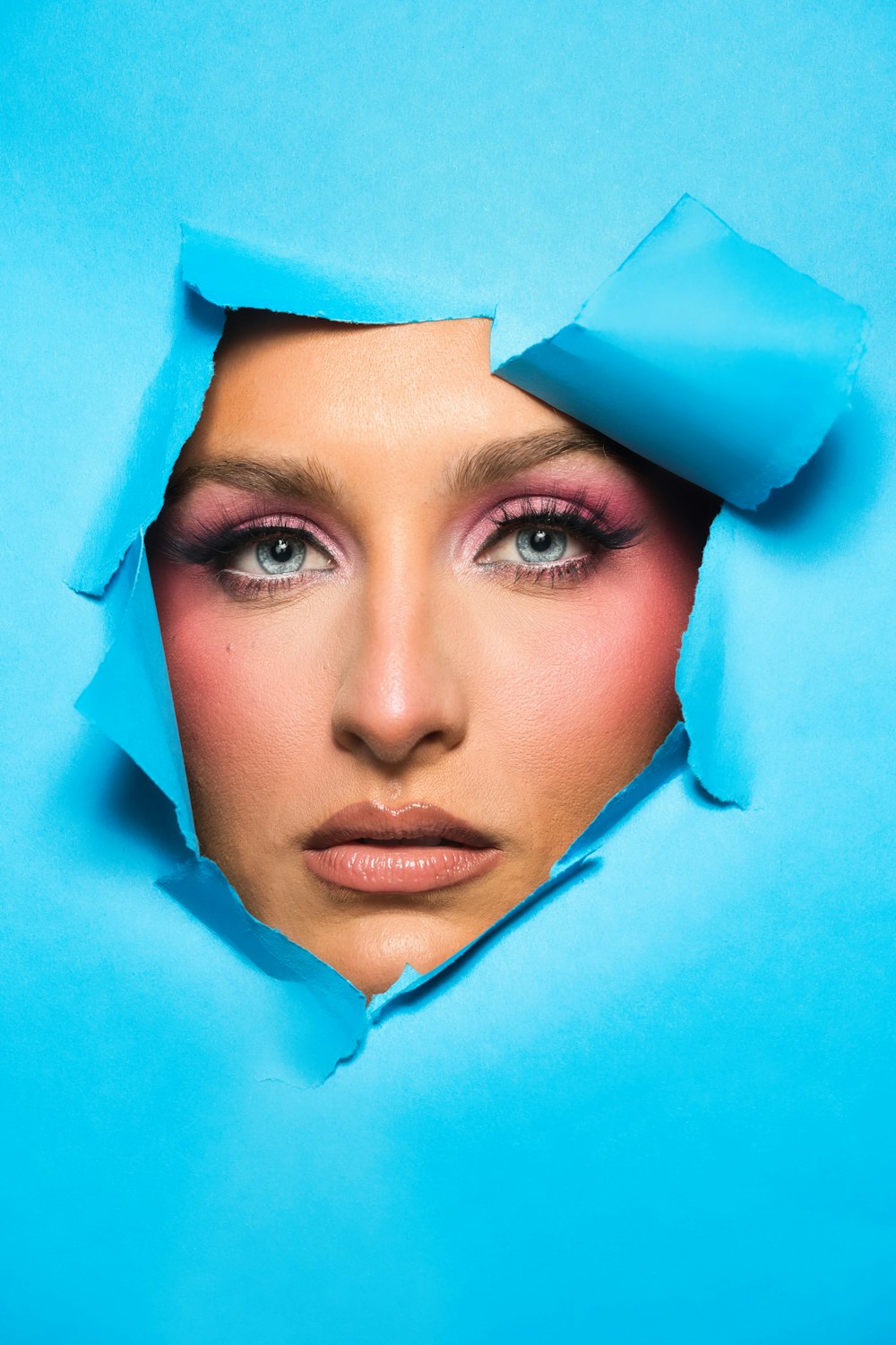 a woman's face is seen through a hole in blue paper