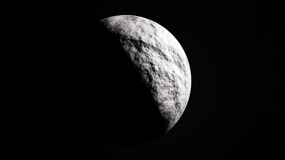 A celestial body with a textured, cratered surface is partially illuminated against a dark, space background. The lighting creates a stark contrast between the bright and shadowed areas, enhancing the planet's spherical shape.