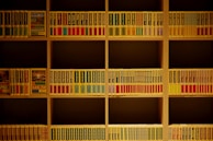 A colorful stack of books in red, blue, yellow, and green arranged on a wooden shelf.