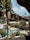 The image portrays a picturesque outdoor scene featuring a swimming pool surrounded by various types of plants, including cactus and palm trees. A prominent rock formation creates a dramatic backdrop, while white, curved architectural elements are integrated into the natural landscape.