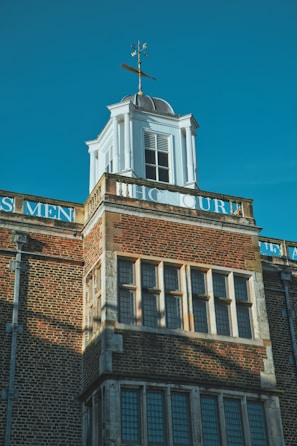 A historic building with classic architectural elements, featuring brickwork and a white cupola topped with a weather vane. The word 'HONOUR' is partially visible, painted in white against the brick. The building has large rectangular windows, and the overall composition conveys a sense of tradition and permanence.