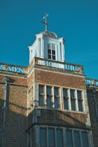 A historic building with classic architectural elements, featuring brickwork and a white cupola topped with a weather vane. The word 'HONOUR' is partially visible, painted in white against the brick. The building has large rectangular windows, and the overall composition conveys a sense of tradition and permanence.