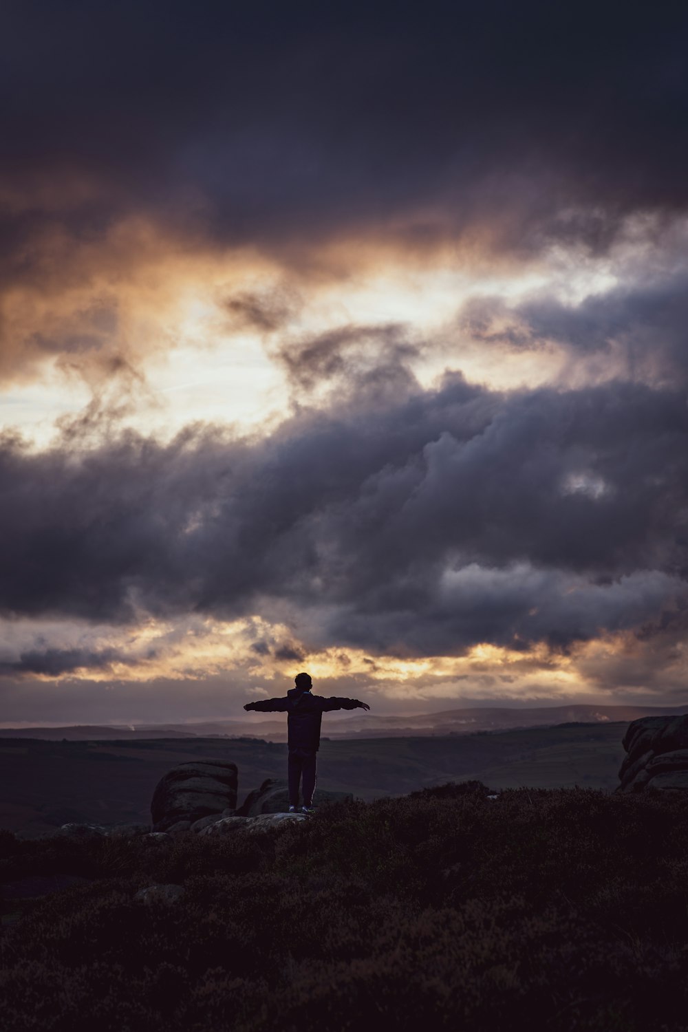 a man standing on top of a hill under a cloudy sky