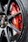 A close-up shot of a red Brembo brake caliper mounted on a dark alloy wheel of a vehicle. The metallic surface of the wheel complements the vibrant red of the caliper, which bears the white Brembo logo. The background shows part of the brake disc.