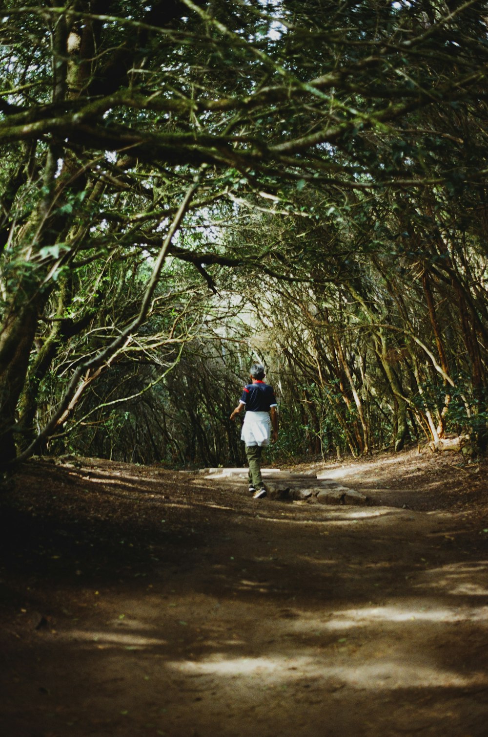 a man walking down a dirt road surrounded by trees