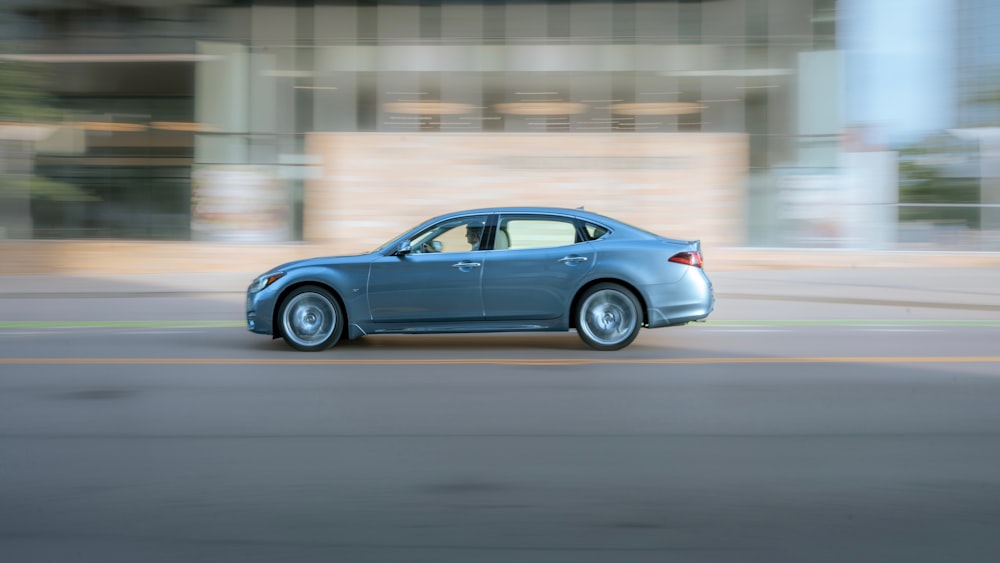 a blue car driving down a street next to a tall building