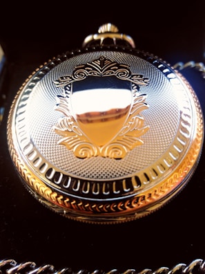 An ornate Victorian pocket watch resting on a velvet cushion, its intricate gears visible through a glass back.