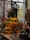 A vibrant display of various flowers and plants, including red, yellow, and green floral arrangements. Large dried plants and berries are visible in the background, creating a rustic ambiance. Glass vases and decorative gourds are arranged on a wooden table, accompanied by other garden and home accessories.