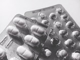 Blister packs containing tablets and pills, arranged overlapping on a flat surface. The image is in black and white, highlighting texture and form.