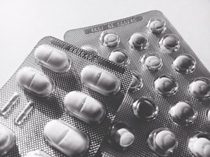 Blister packs containing tablets and pills, arranged overlapping on a flat surface. The image is in black and white, highlighting texture and form.