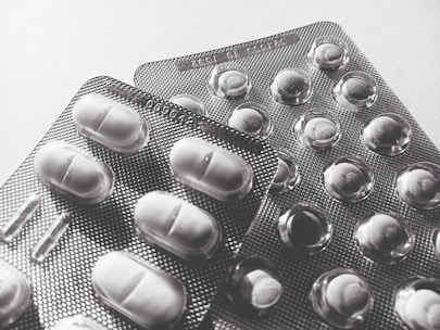 Blister packs containing tablets and pills, arranged overlapping on a flat surface. The image is in black and white, highlighting texture and form.