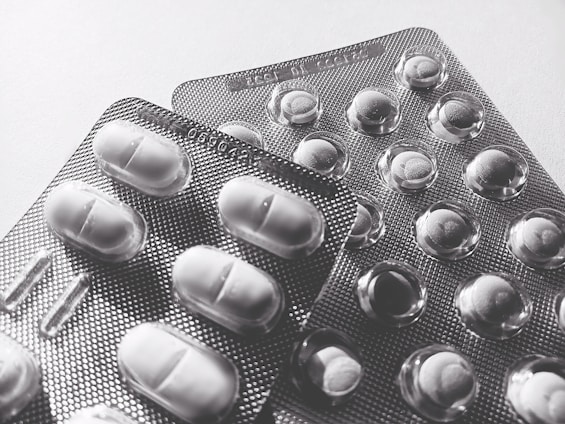 Blister packs containing tablets and pills, arranged overlapping on a flat surface. The image is in black and white, highlighting texture and form.