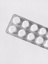 A silver blister pack containing white round pills, placed on a clean, plain background. The packaging is textured and reflective, and each pill is separated in its own compartment.