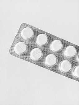 A silver blister pack containing white round pills, placed on a clean, plain background. The packaging is textured and reflective, and each pill is separated in its own compartment.